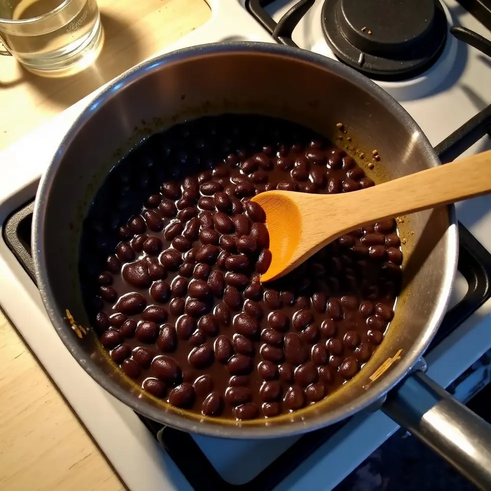 Black beans simmering in saucepan with wooden spoon, liquid reducing on stovetop