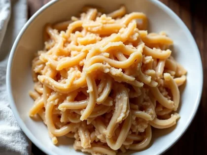 Shredded chicken breast in a white bowl, golden-tan strands coated with cooking liquid on a wooden surface